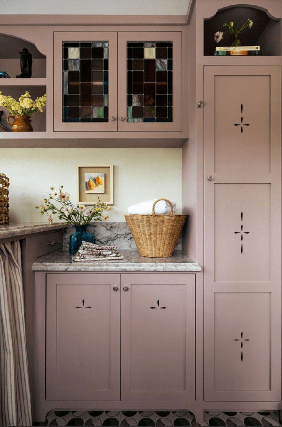 Purple cabinets with decorative glass, marble counter, and basket with rolled towel.