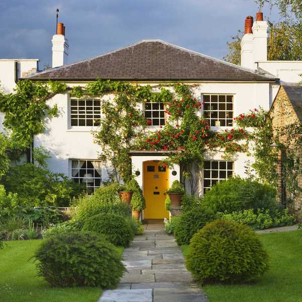 Quaint cottage with a bright yellow door, vines, and a lush garden path.