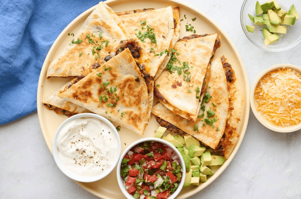 Quesadilla slices with sour cream, salsa, avocado, and cheese on a plate.