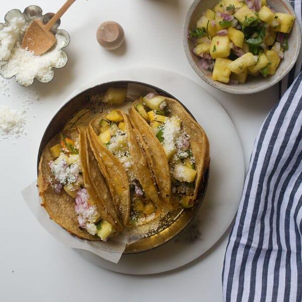 quesataco and pineapple salsa on a cream colored plate beside a navy and white striped napkin