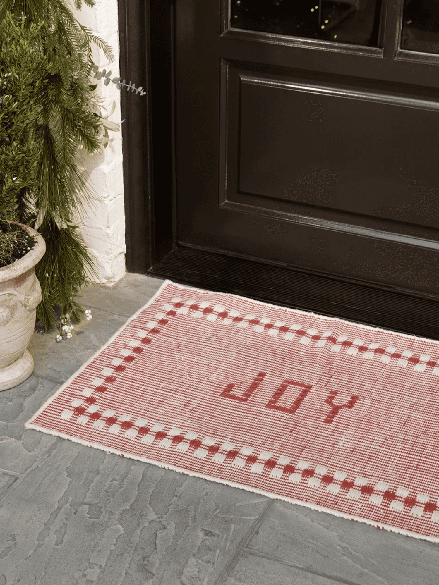 Red and white doormat with "JOY" at a doorway next to a potted plant.