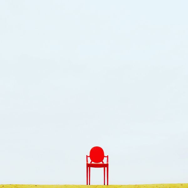 red chair in the middle of a green field and blue sky