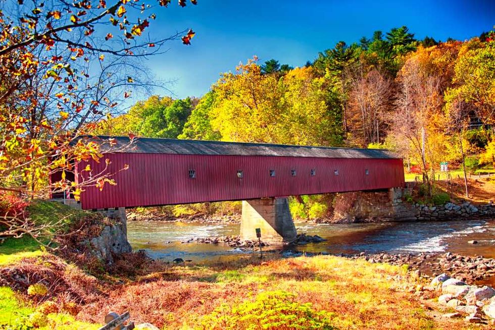 Red covered bridge over a stream, surrounded by colorful autumn foliage.
