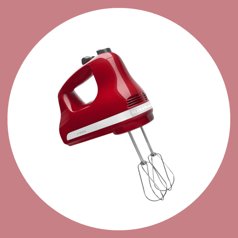 Red electric hand mixer with beaters, white circle, pink background.