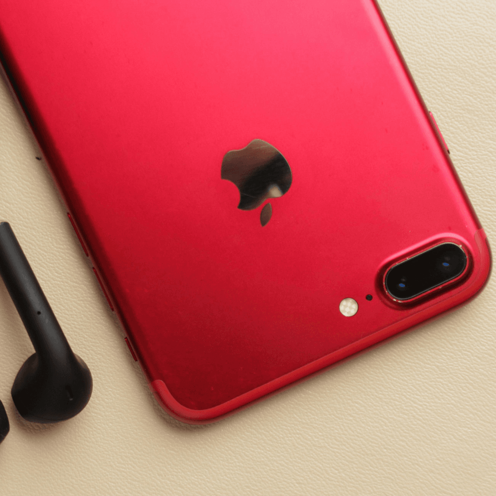 Red iPhone with black earbuds on a ivory background