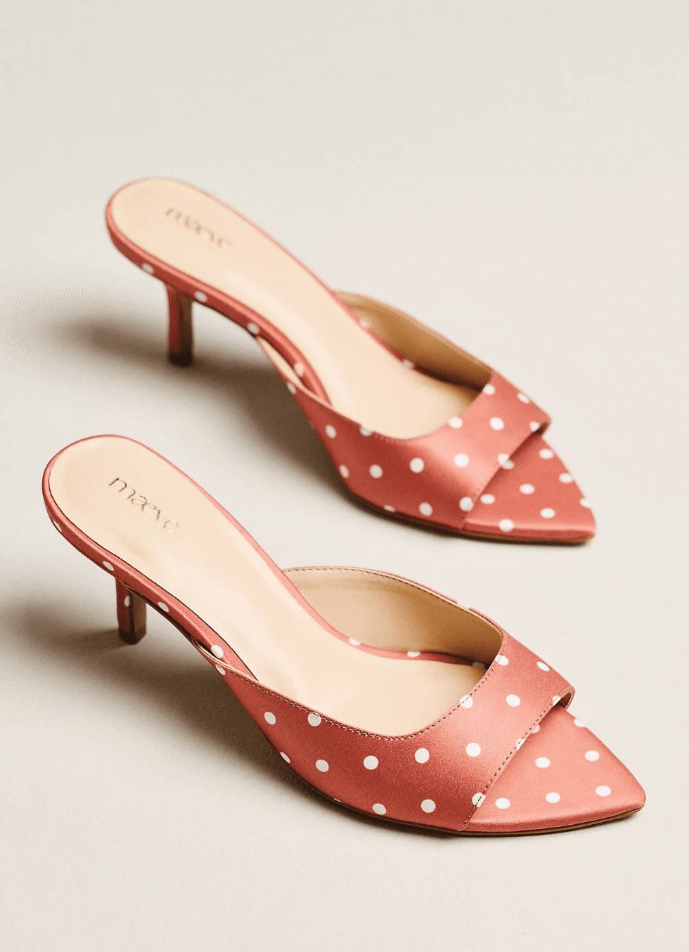 Red polka dot heeled mules on a neutral background.