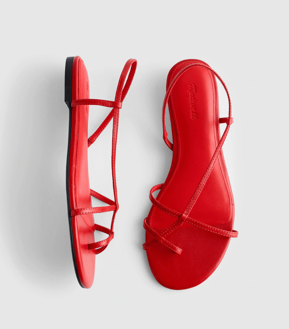 Red sandals with thin straps, black soles, on a light gray background.
