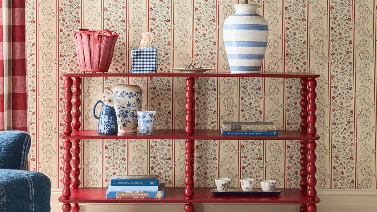 Red shelf with decorative items against floral wallpaper.