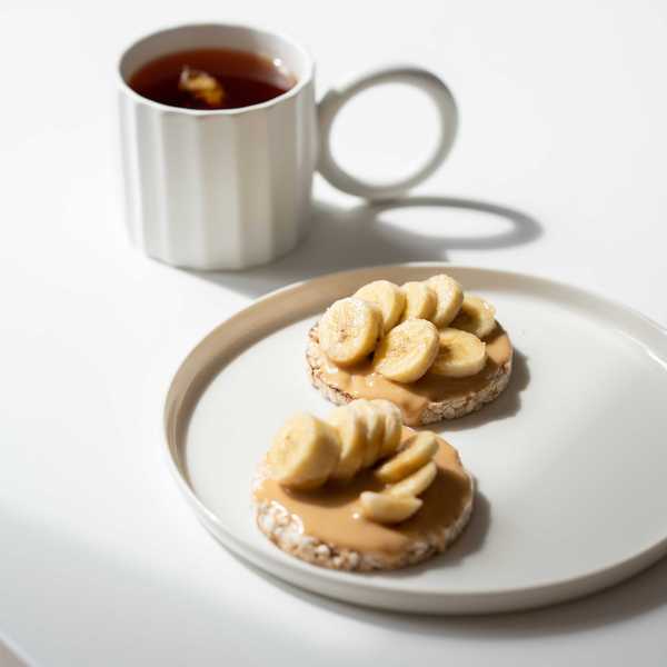 Rice cakes with peanut butter and banana, next to a mug of tea.