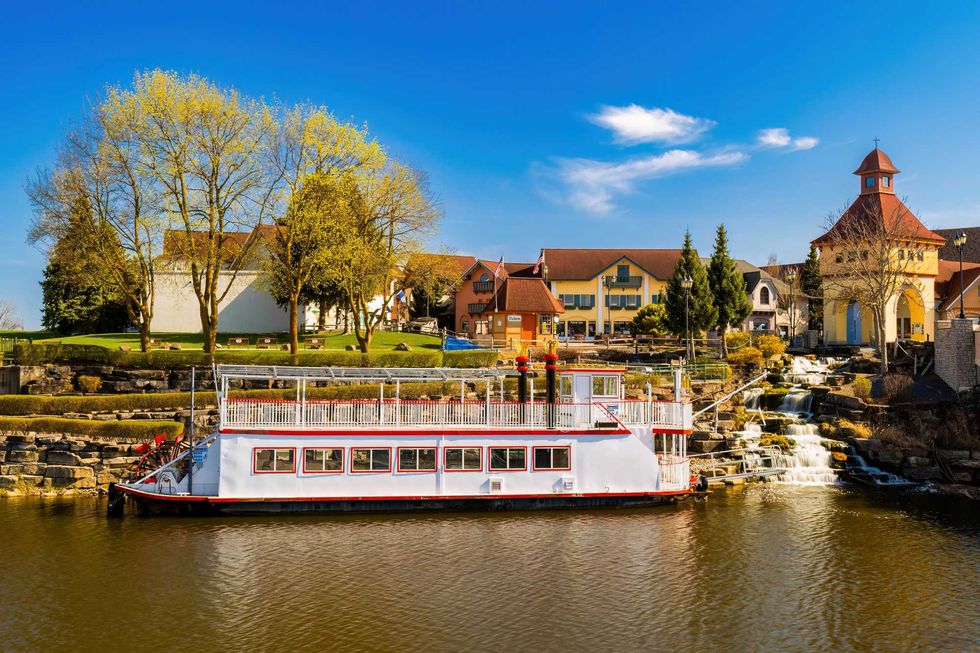 Riverboat docked near a quaint village with a church and waterfall.