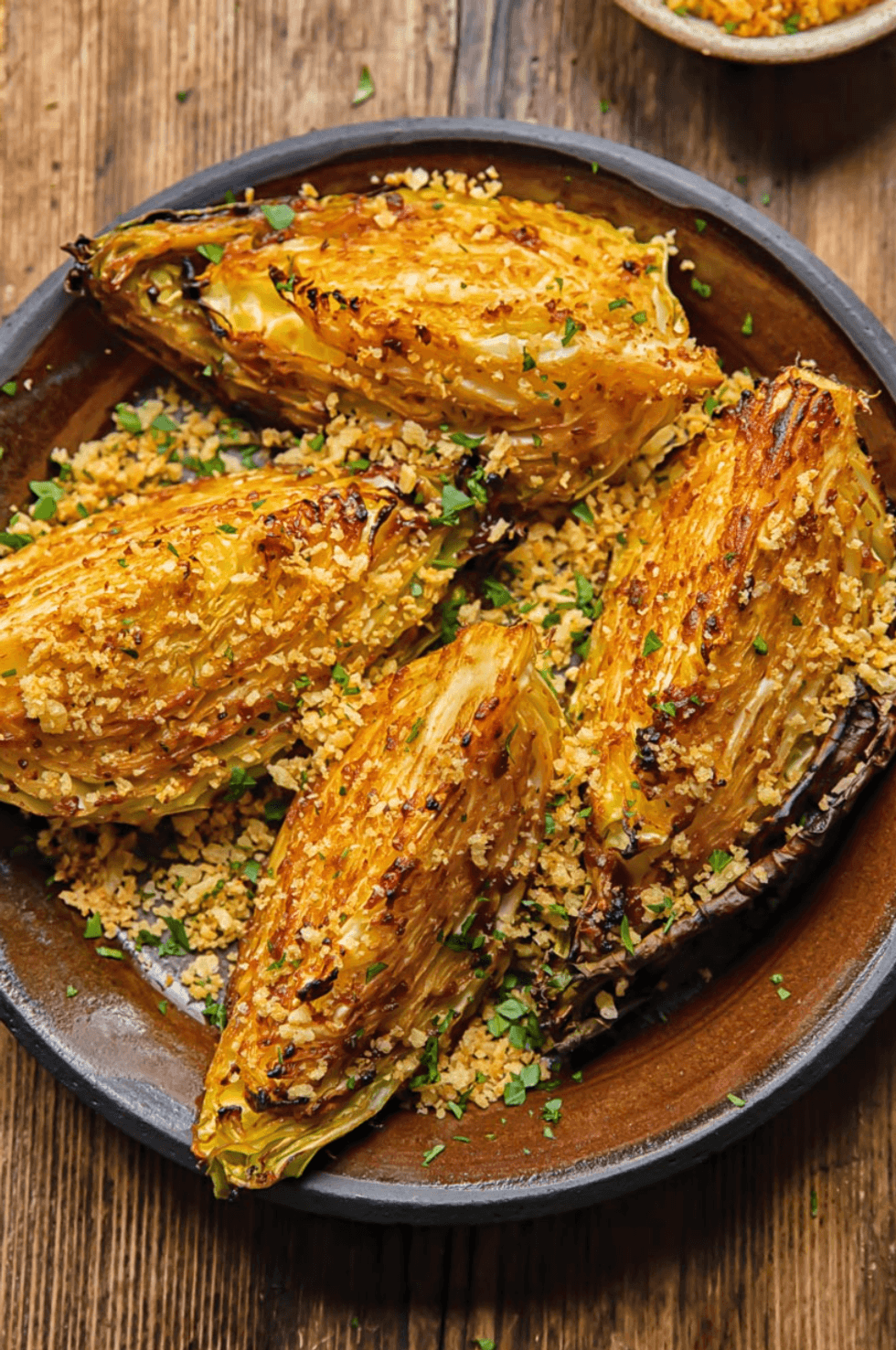 Roasted cabbage wedges with crispy panko and parsley on a wooden table.