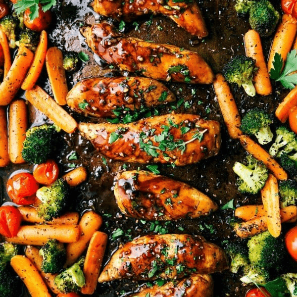 Roasted chicken with carrots, broccoli, and tomatoes, garnished with herbs.