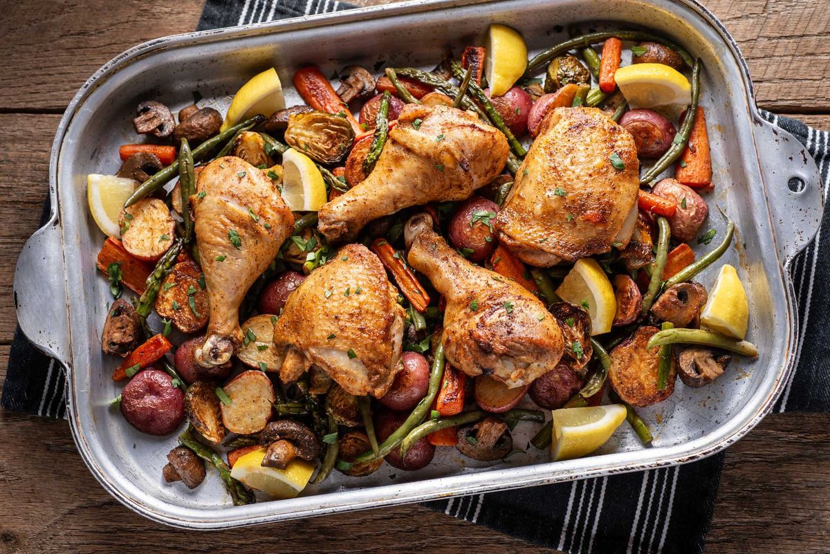 Roasted chicken with vegetables and lemon wedges in a large baking dish.