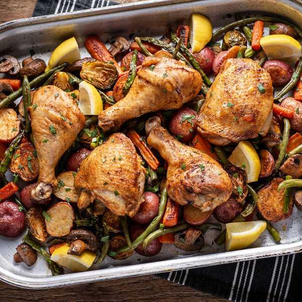 Roasted chicken with vegetables and lemon wedges in a large baking dish.