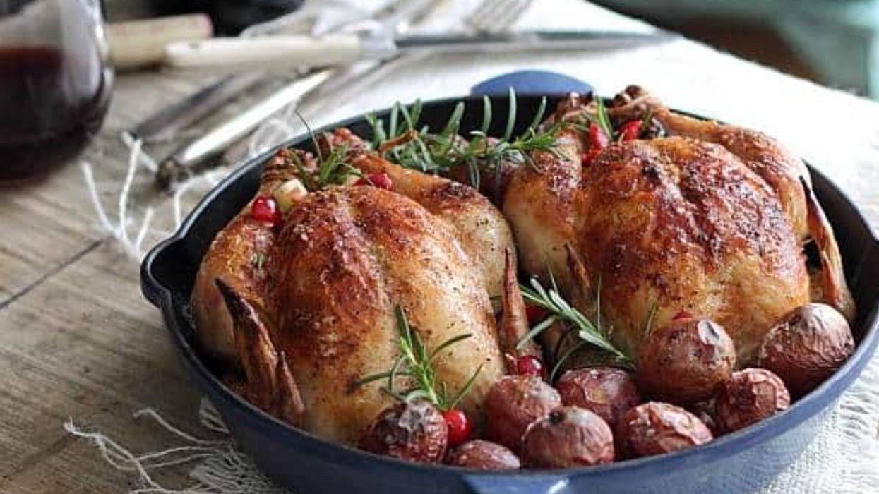 Roasted chickens with potatoes and herbs in a skillet, served with red wine on a rustic table.