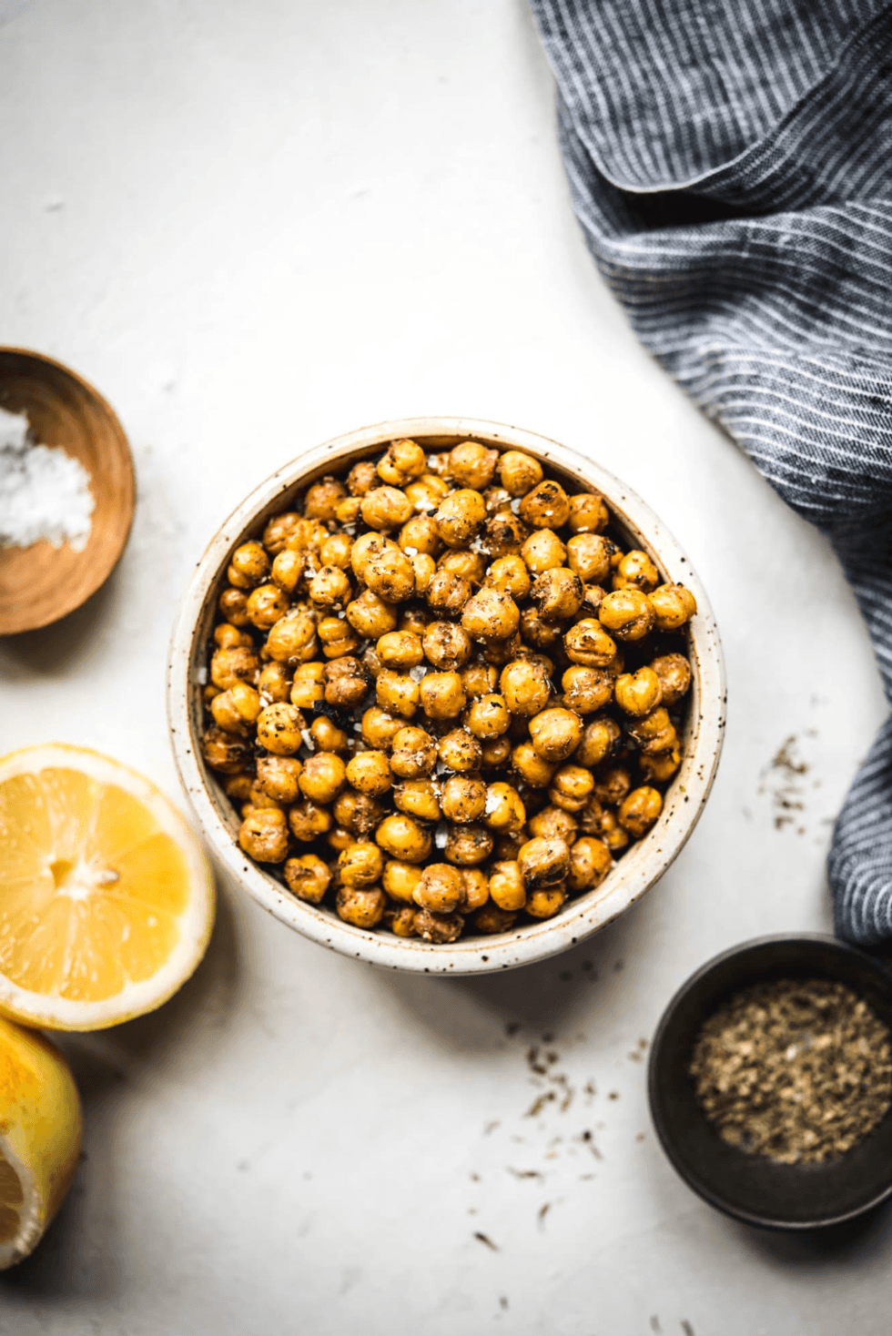 Roasted chickpeas in a bowl with lemon slices and spices on a table.