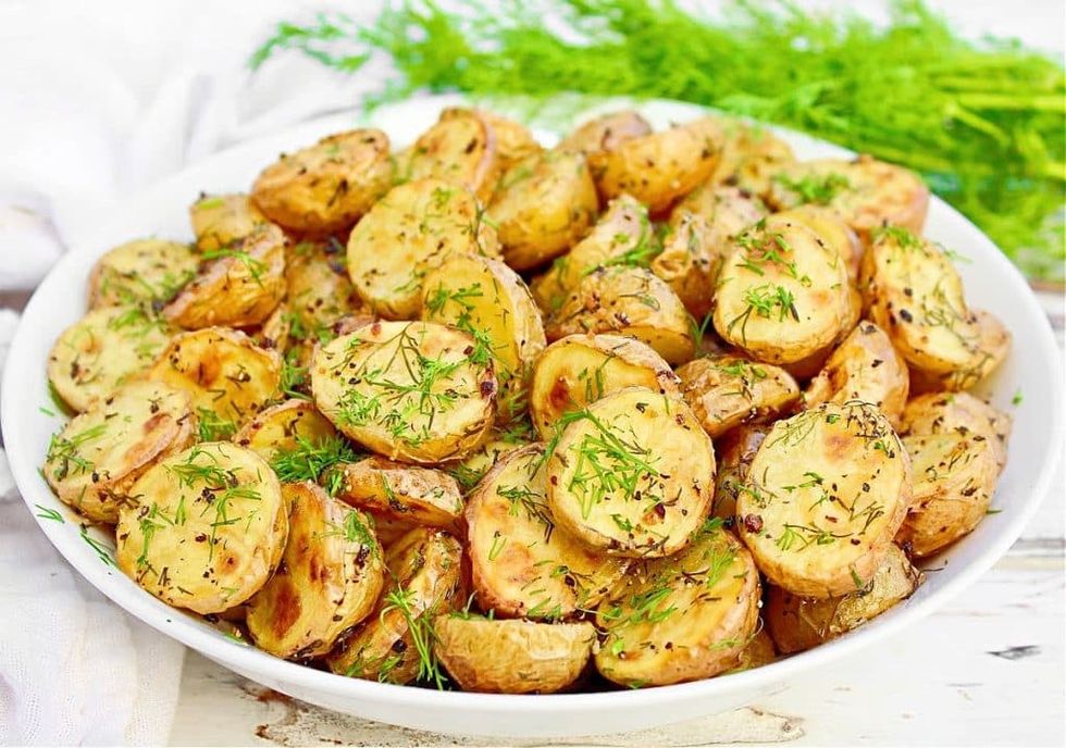 Roasted dill potatoes sit inside of a white bowl.