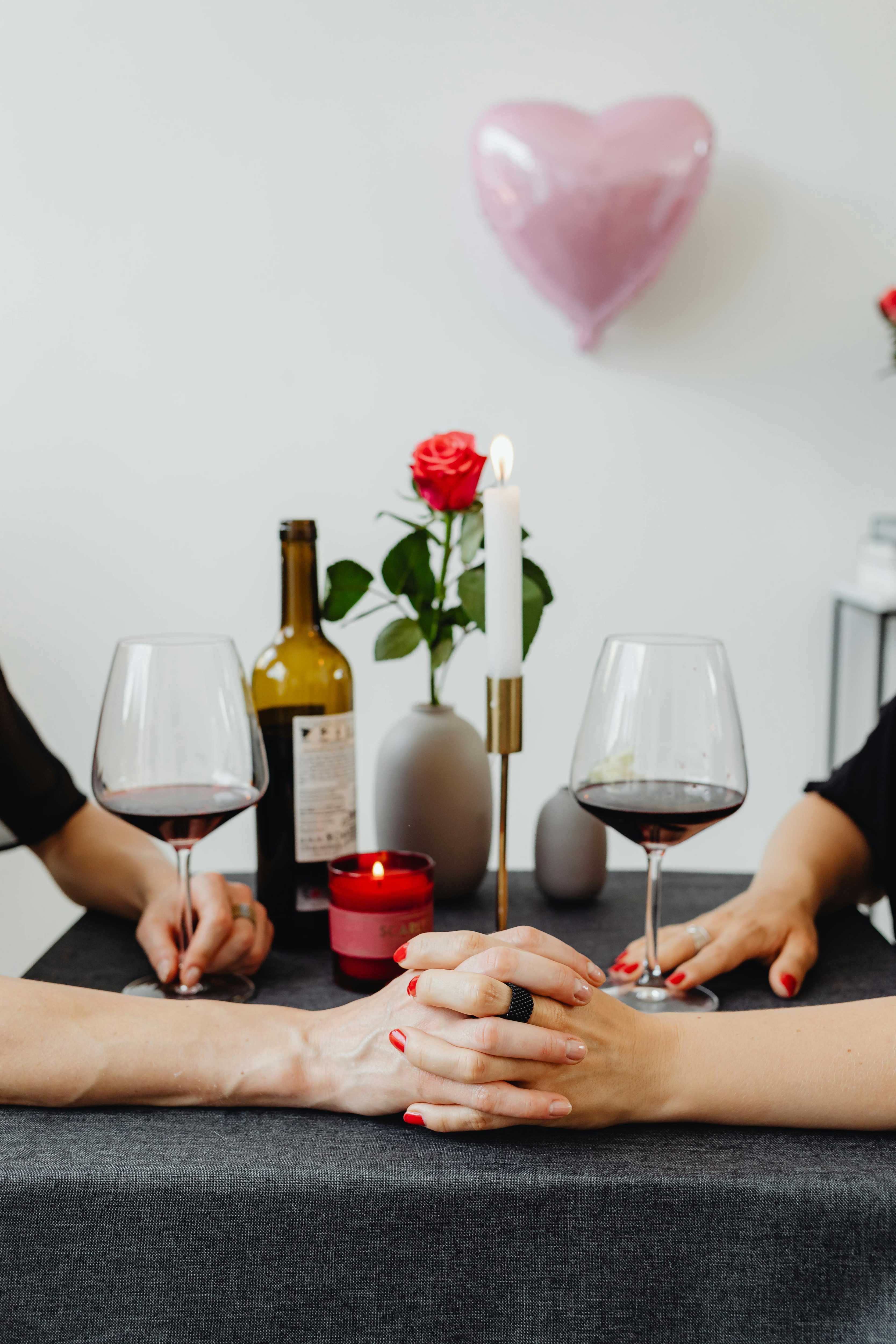 Romantic dinner with wine, candle, rose, and a couple holding hands at a table.