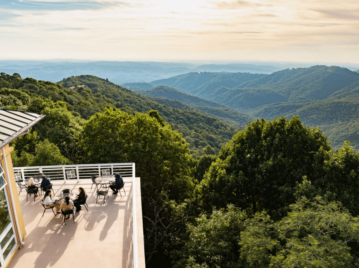 Rooftop patio with people enjoying mountain views under a cloudy sky.