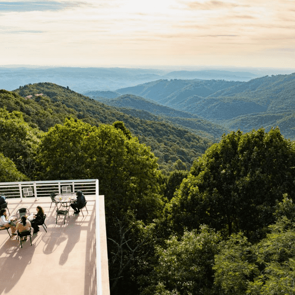 Rooftop patio with people enjoying mountain views under a cloudy sky.