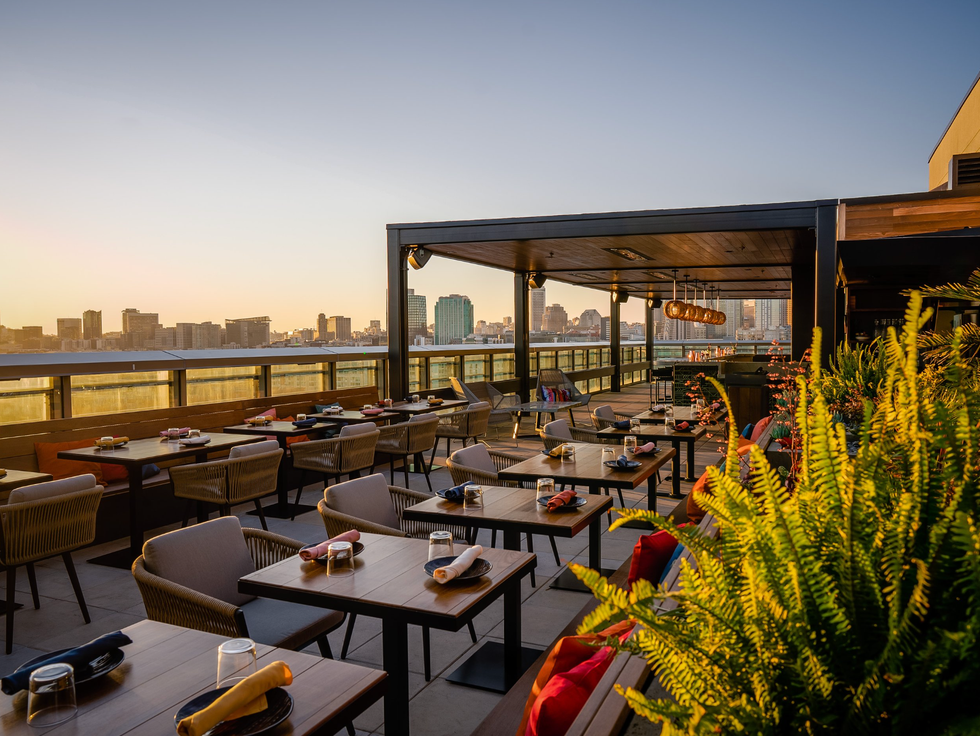 Rooftop restaurant at sunset with city skyline views and greenery.