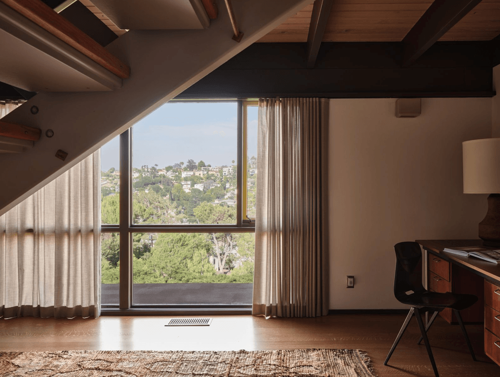 Room with large window view of greenery, desk, chair, and staircase.