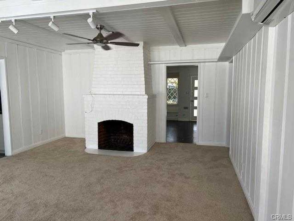 Room with white brick fireplace, beige carpet, wood panel walls, and ceiling fan.