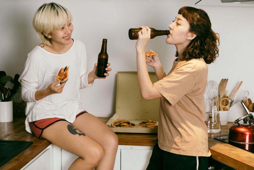 roommates drinking beer and eating pizza in kitchen