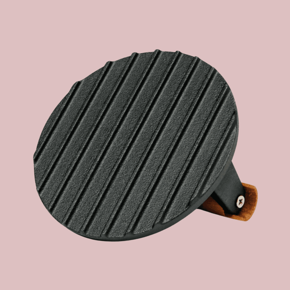 Round, black, ribbed cast iron grill press on a pink background.
