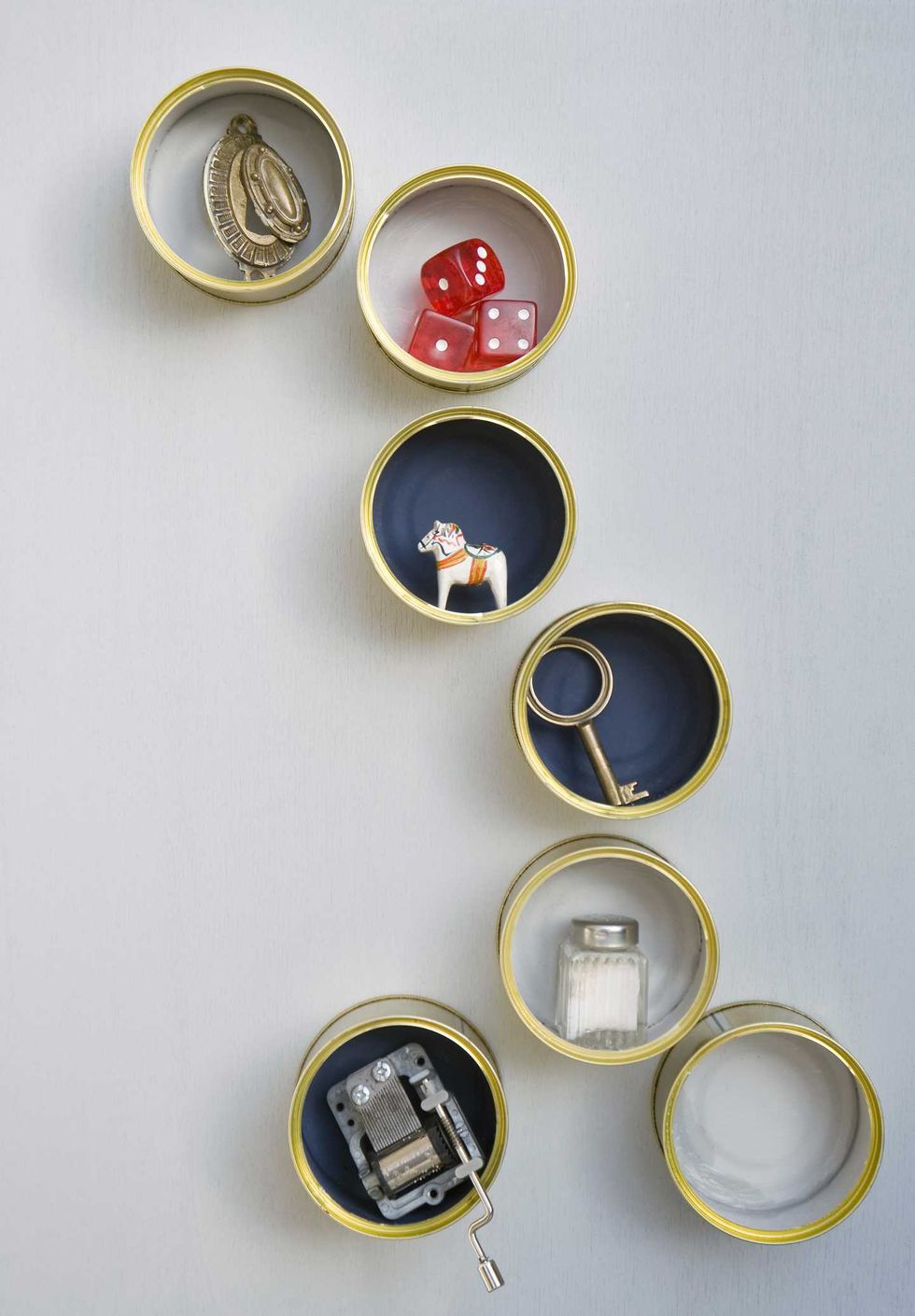 Round containers with trinkets: medal, dice, figure, key, salt shaker, music box.