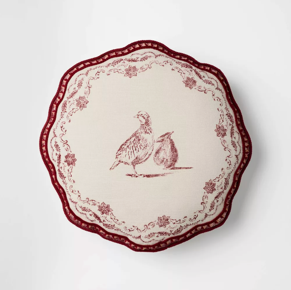 Round cushion with red bird and floral design on cream fabric.