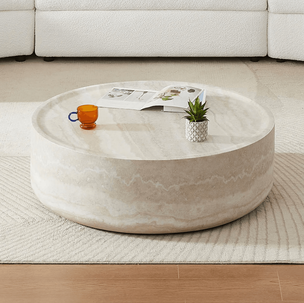 Round stone coffee table with a magazine, orange cup, and small potted plant.