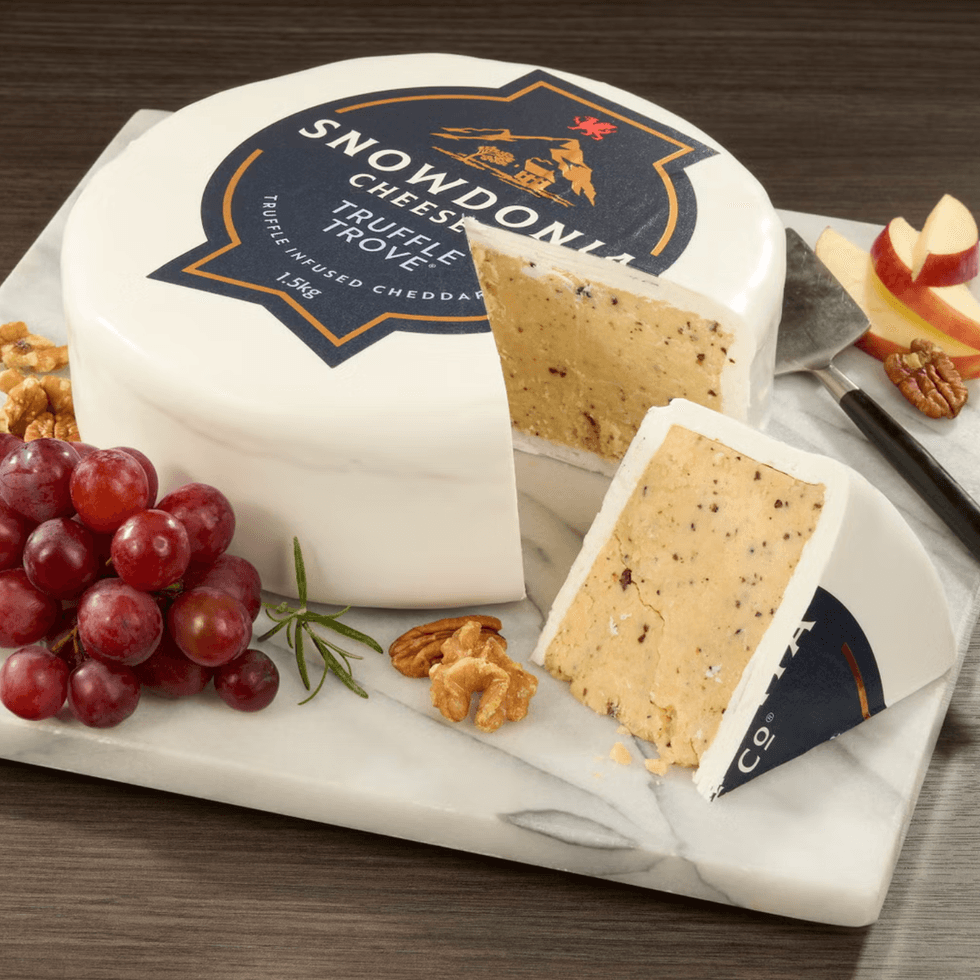 Round truffle cheese on marble with grapes, apple slices, and walnuts.