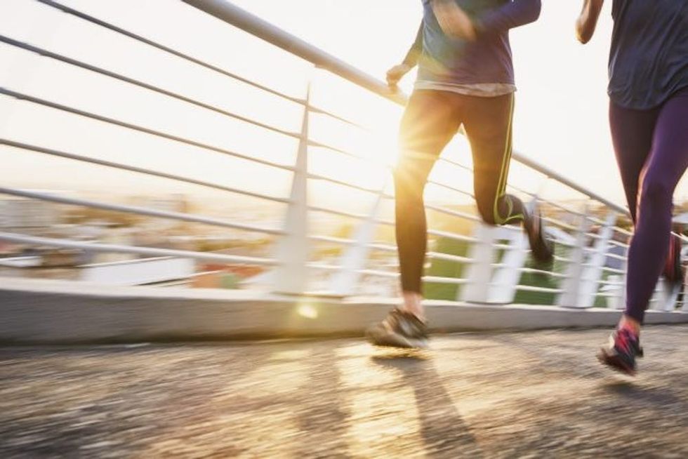 Runner couple running on sunny urban footbridge at sunrise