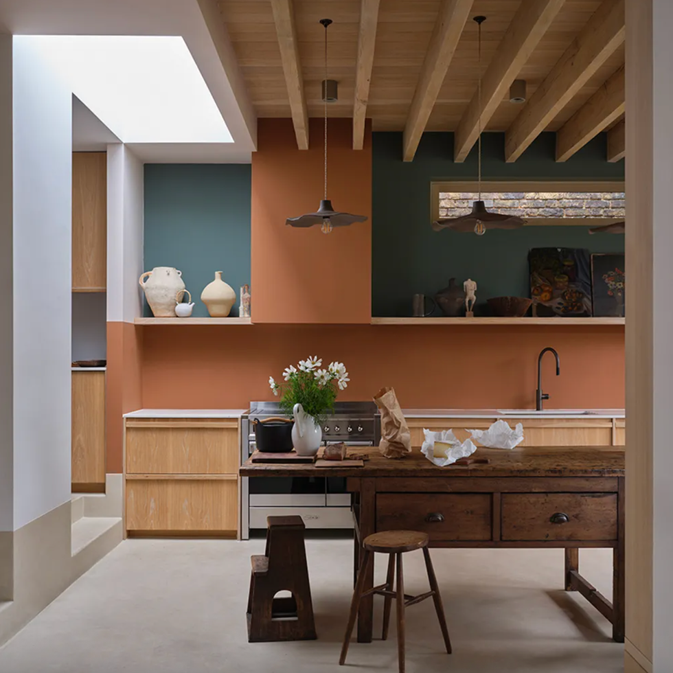 Rustic kitchen with wooden beams, teal and terracotta walls, and vintage wooden table.