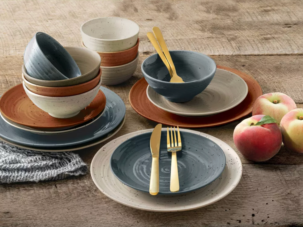 Rustic tableware with peaches on a wooden table alongside golden cutlery.