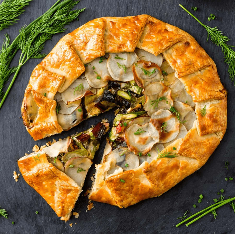 Rustic vegetable galette with a golden crust, garnished with fresh dill on a slate surface.