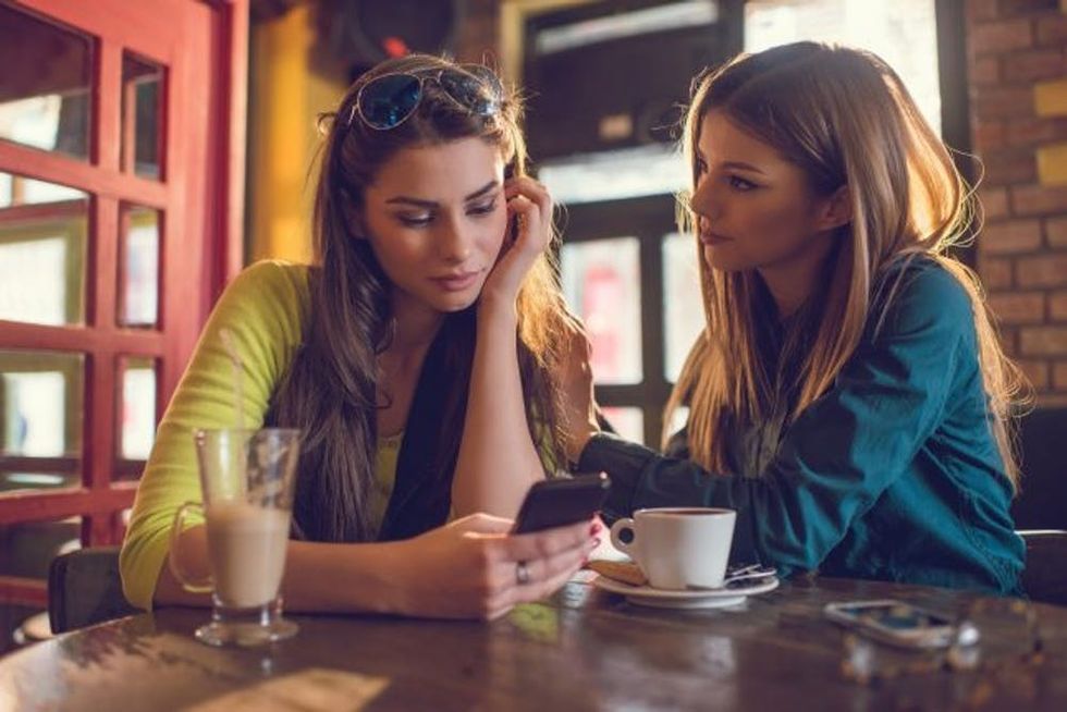 Sad woman reading text message to her friend in cafe.