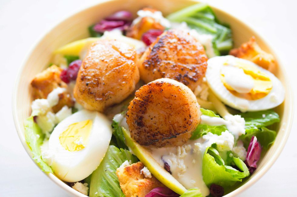 Salad with seared scallops, hard-boiled eggs, lettuce, croutons, and dressing in a bowl.