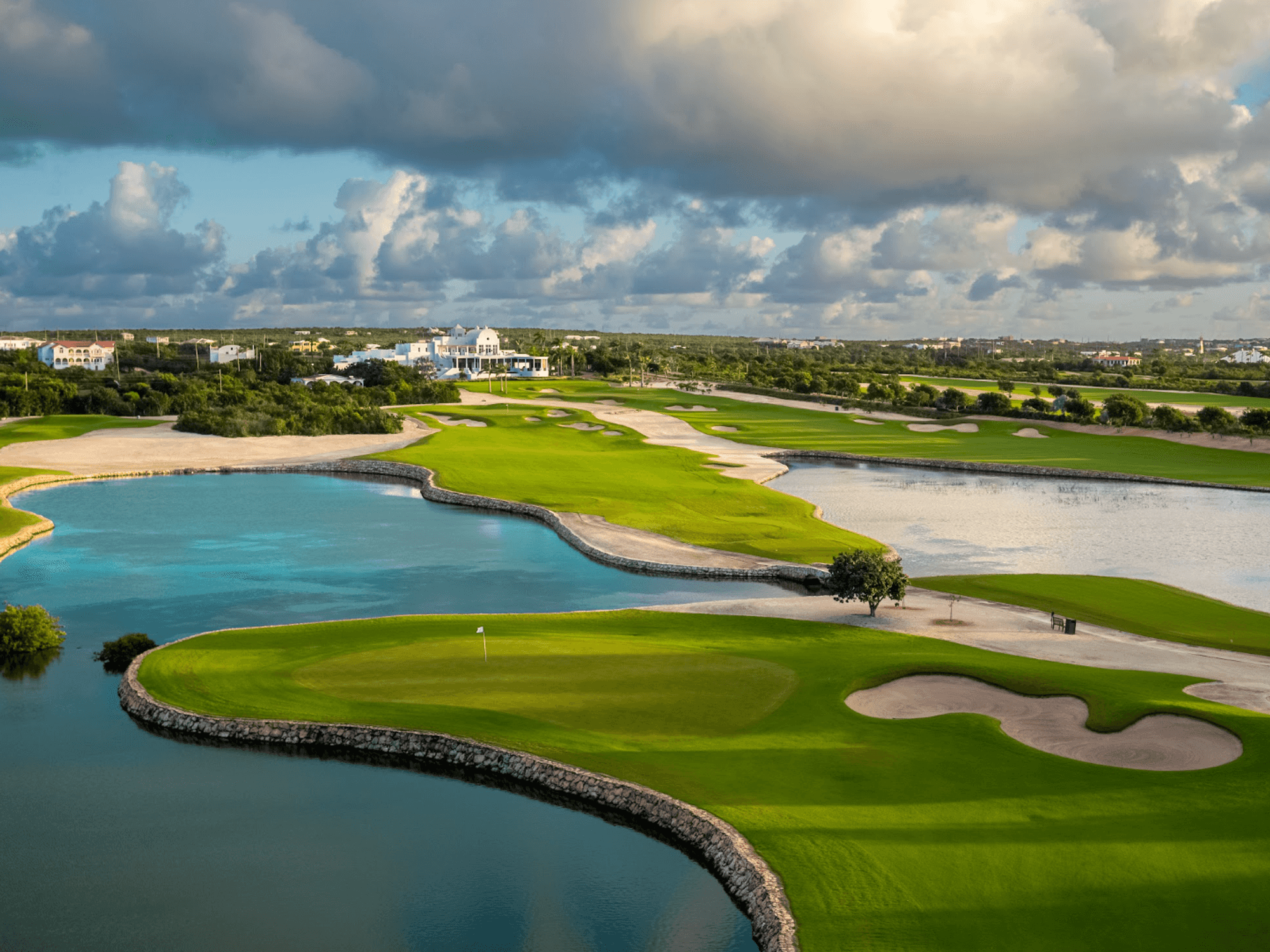 Scenic golf course with water hazards under a cloudy sky.