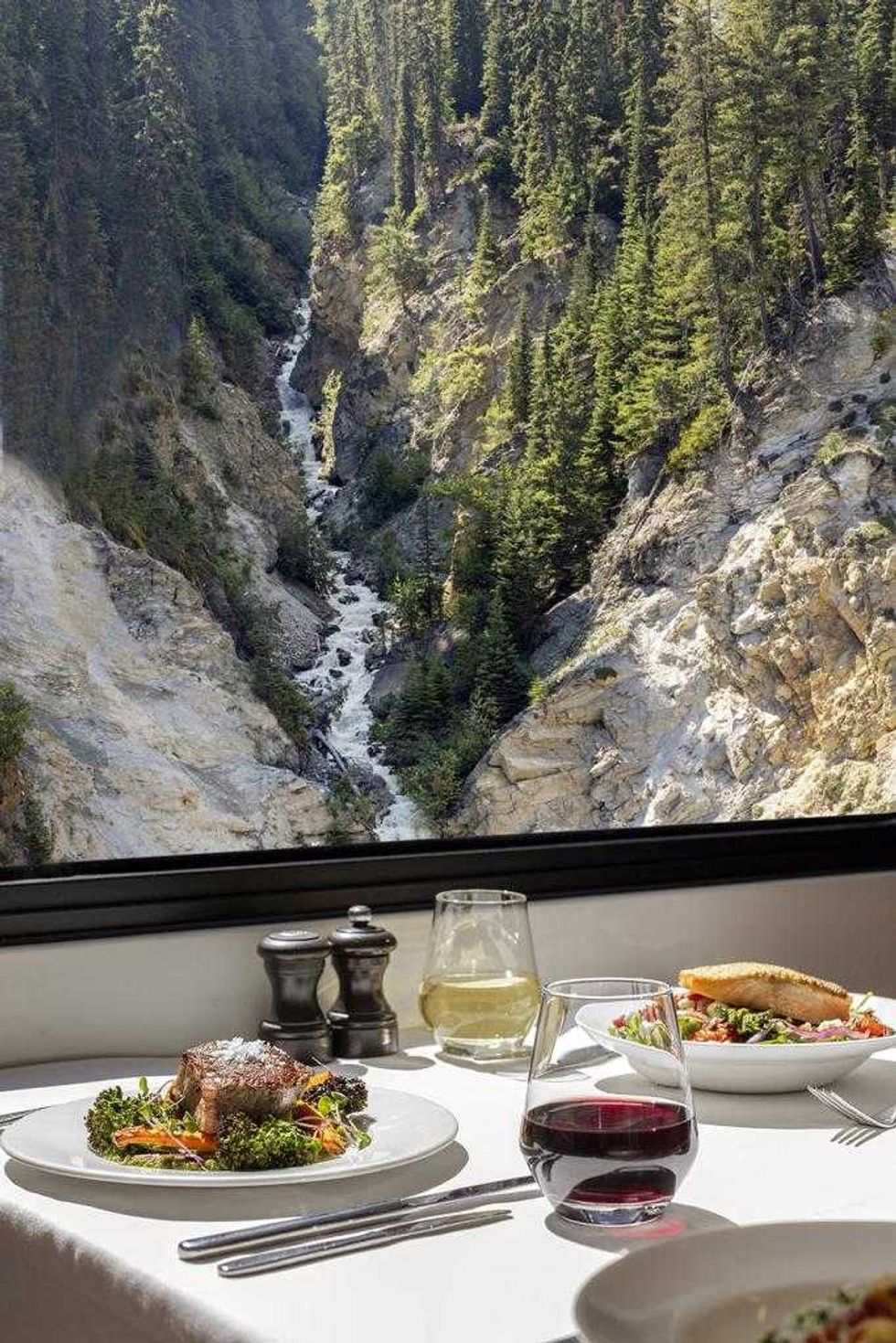 Scenic mountain view from train dining table with gourmet meal and drinks.