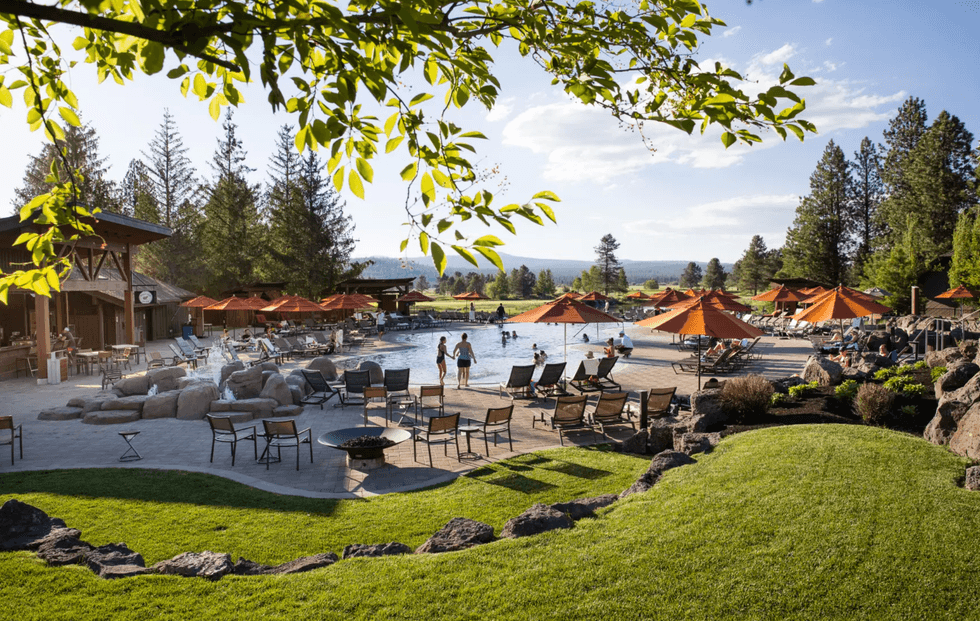 Scenic resort pool with loungers, orange umbrellas, surrounded by trees and lush greenery.