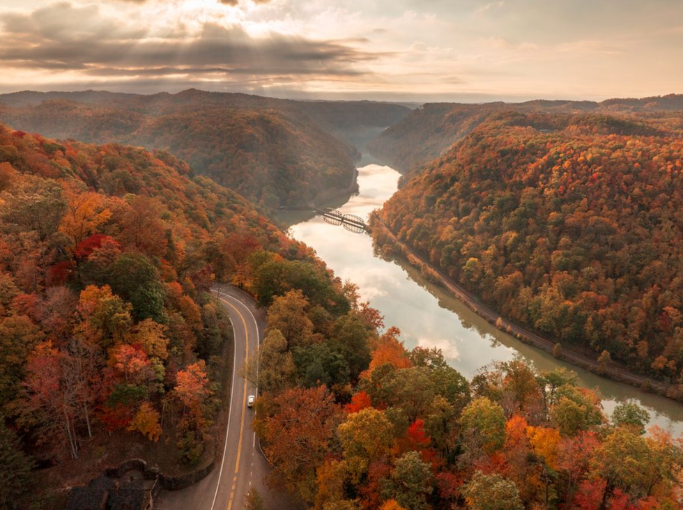 Scenic view of a river and road through vibrant autumnal trees under a cloudy sky.