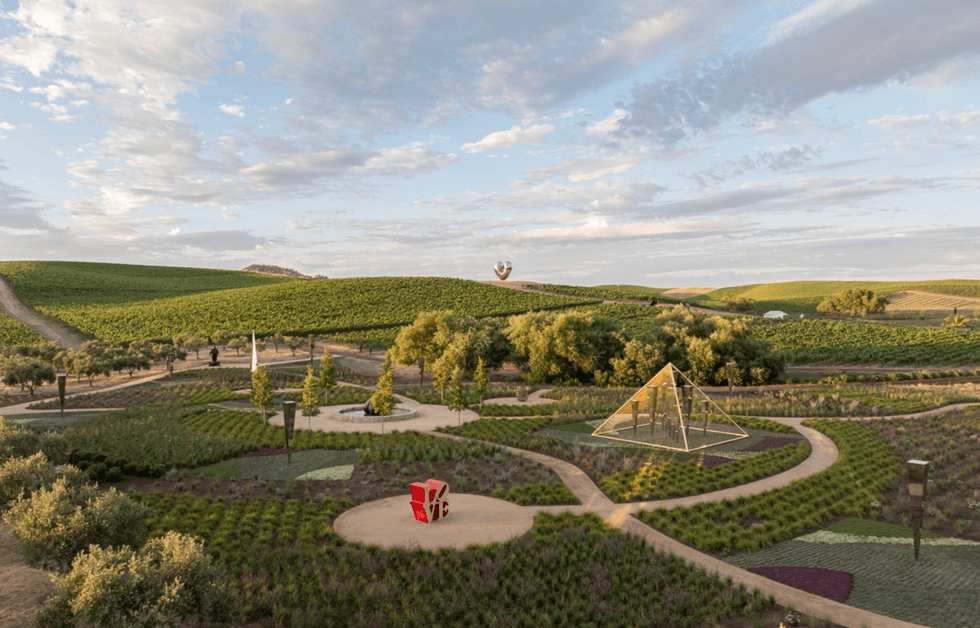 Scenic vineyard landscape with modern sculptures and winding paths under a cloudy sky.