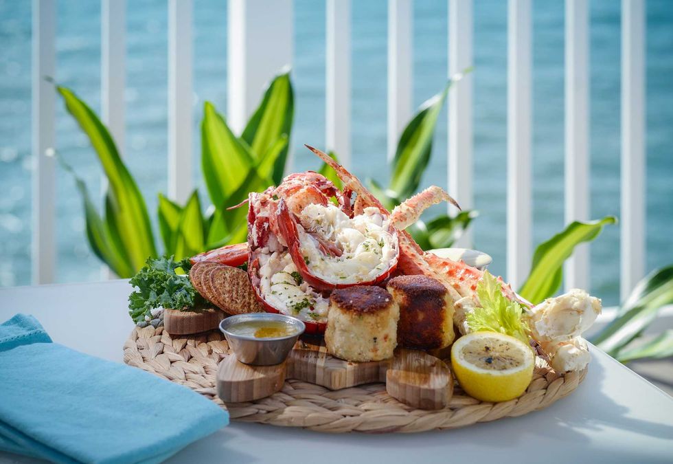 Seafood platter with lobster, crab cakes, lemon slice, and dipping sauce by the ocean.