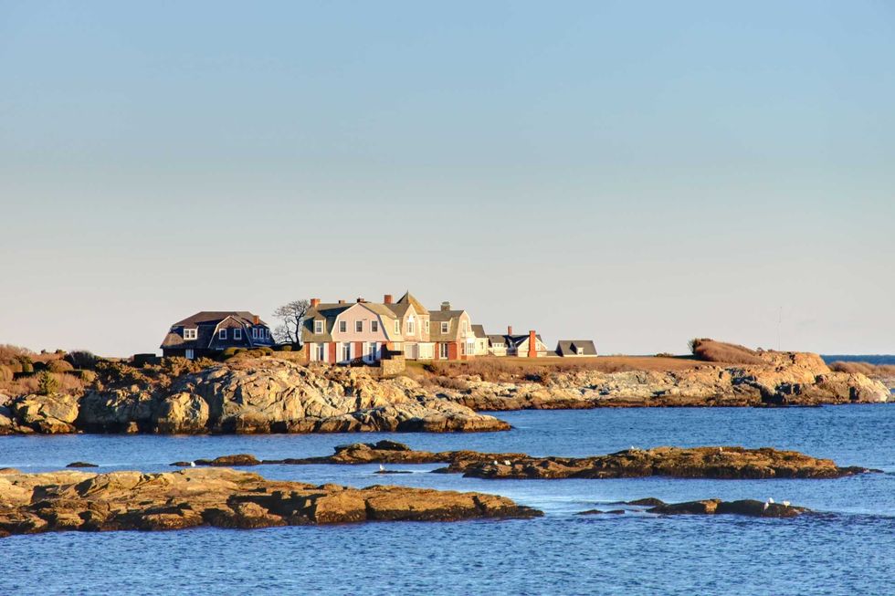 Seaside houses on a rocky shoreline under a clear blue sky.