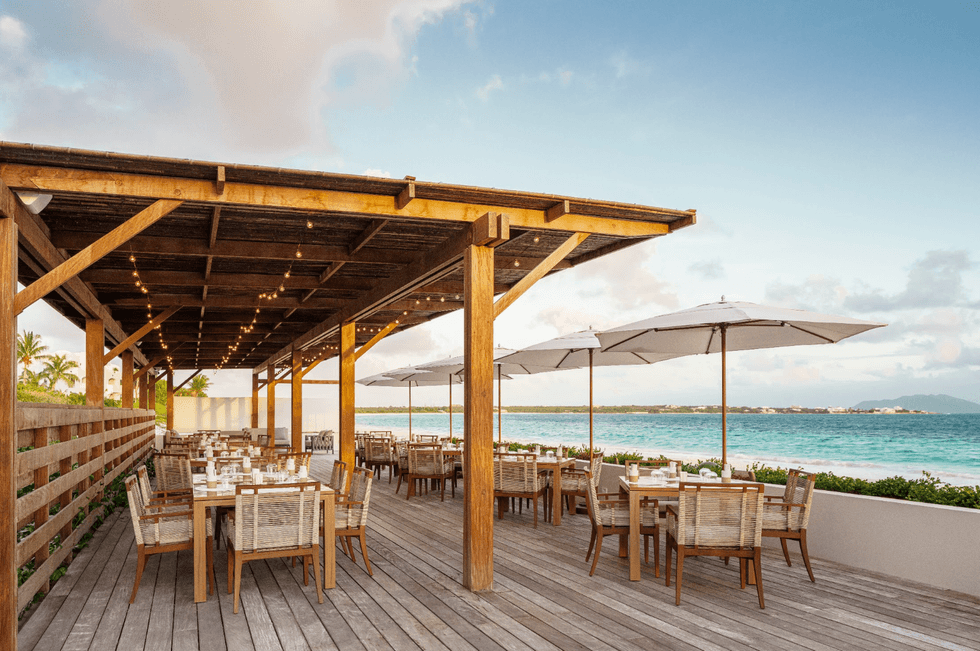 Seaside restaurant patio with wooden tables and umbrellas overlooking the ocean.