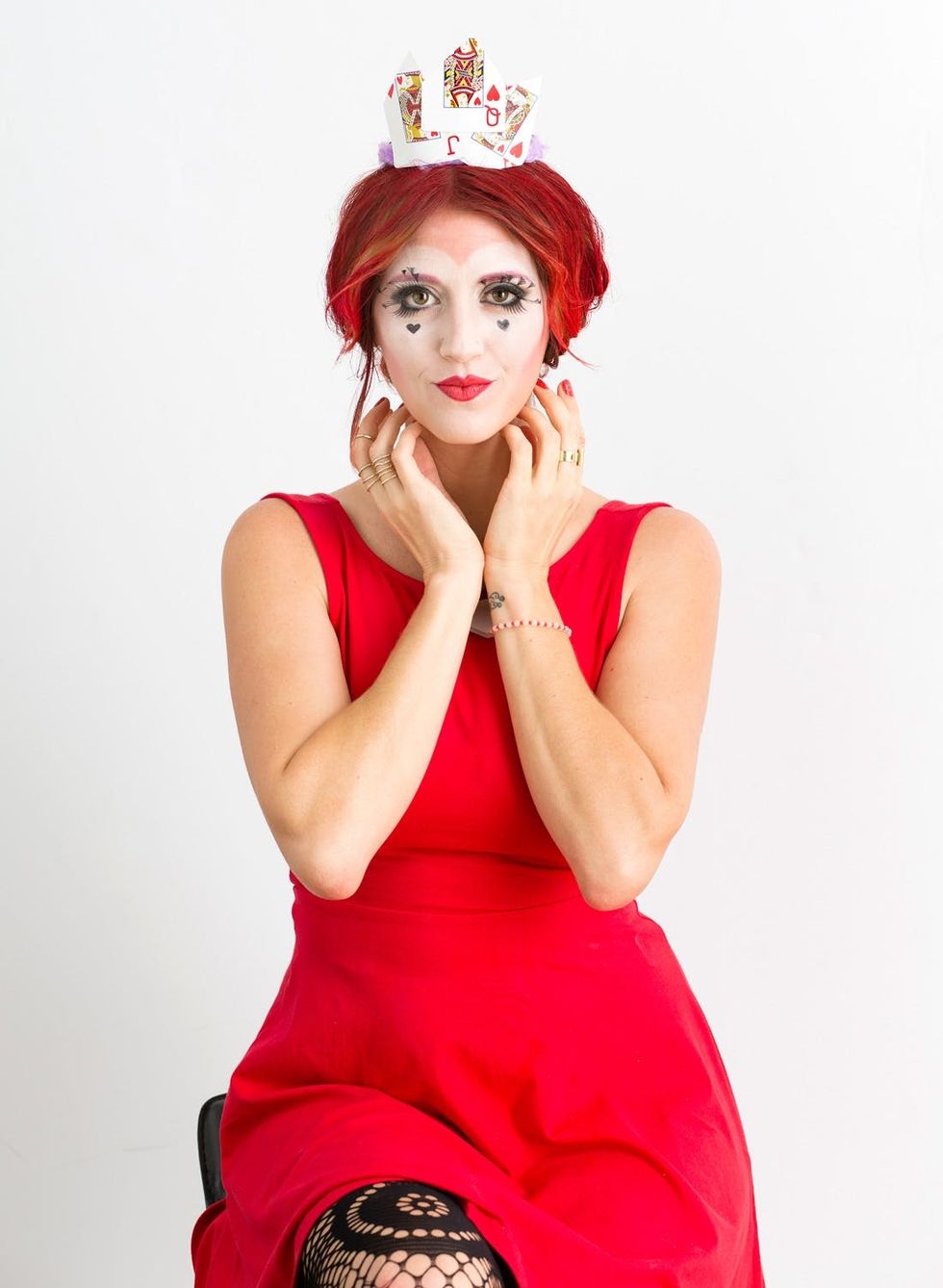 Seated women in red dress with red hair showing off the classic Queen of Hearts makeup and costume