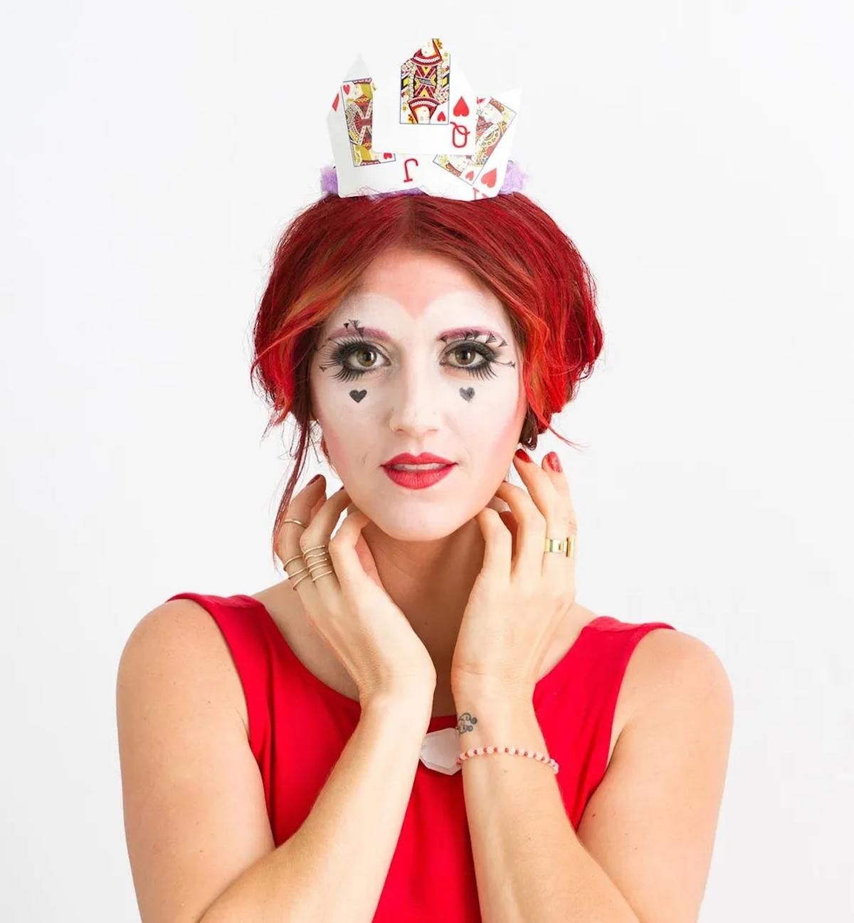 Seated women in red dress with red hair showing off the classic Queen of Hearts makeup and costume