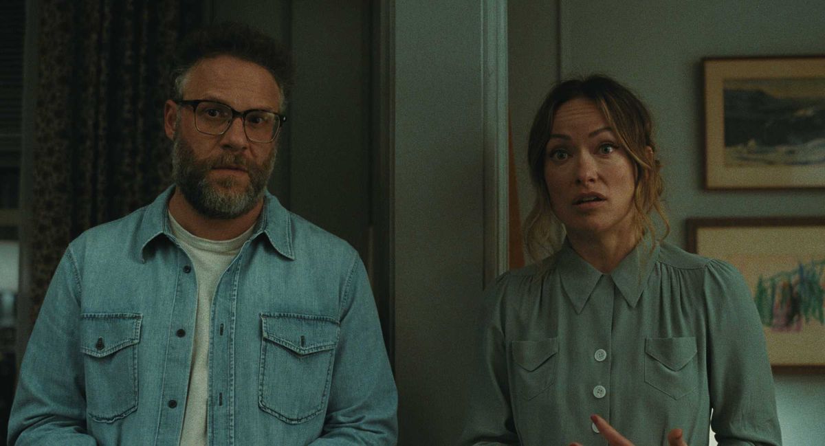 Seth Rogan and Olivia Wilde stand in a room, both appear surprised or concerned.